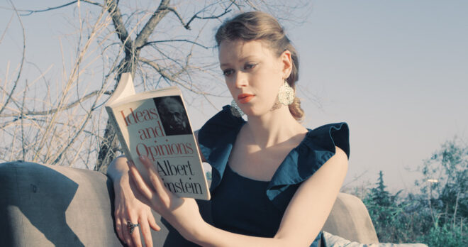 a woman reads a book by Albert Einstein on a sofa outsiden