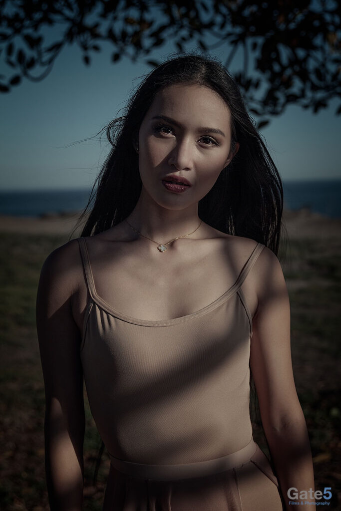 a moody winter portrait of a woman under a tree near the ocean