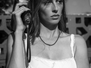 A black and white portrait from the waste up on a young woman holding a super 8mm film camera in front of an old motel.